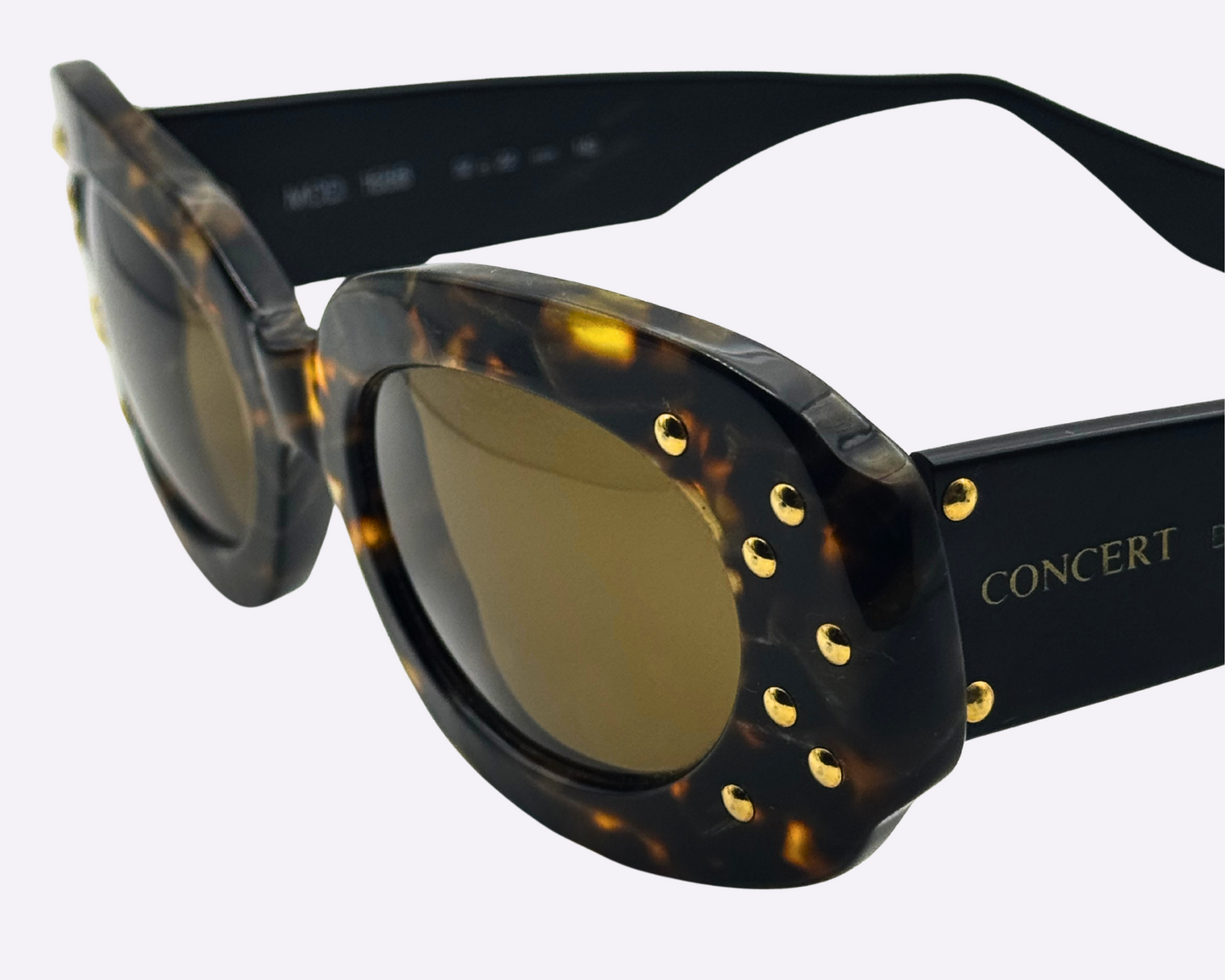 Close-up of vintage Concert sunglasses with brown tortoise frames, highlighting the dazzling gold strass embellishments on the front of the frame, shown on a light gray background.