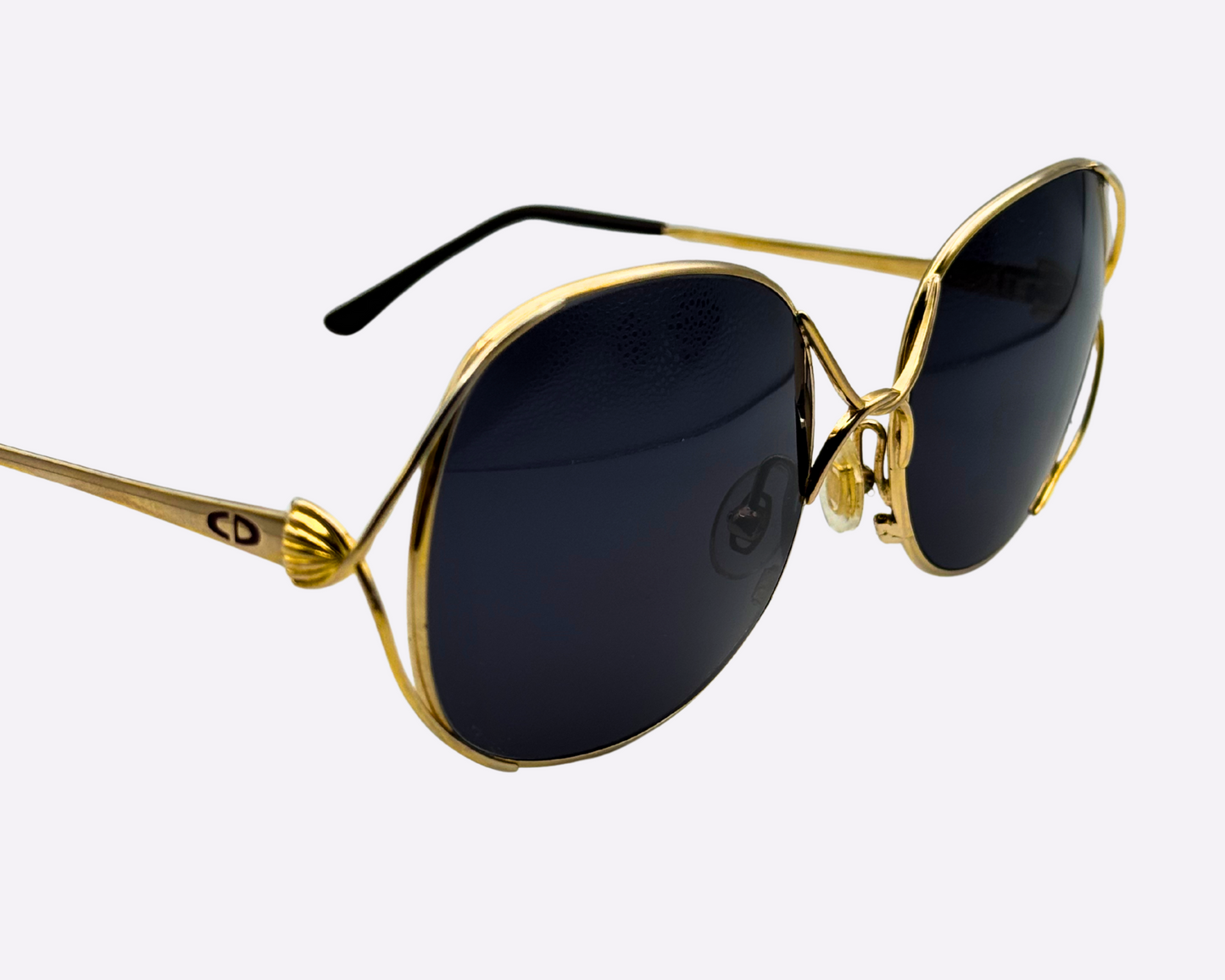 Close-up of the temple and Dior logo on vintage 1980s Christian Dior sunglasses with a steel frame and new grey lenses, shown on a light gray background.