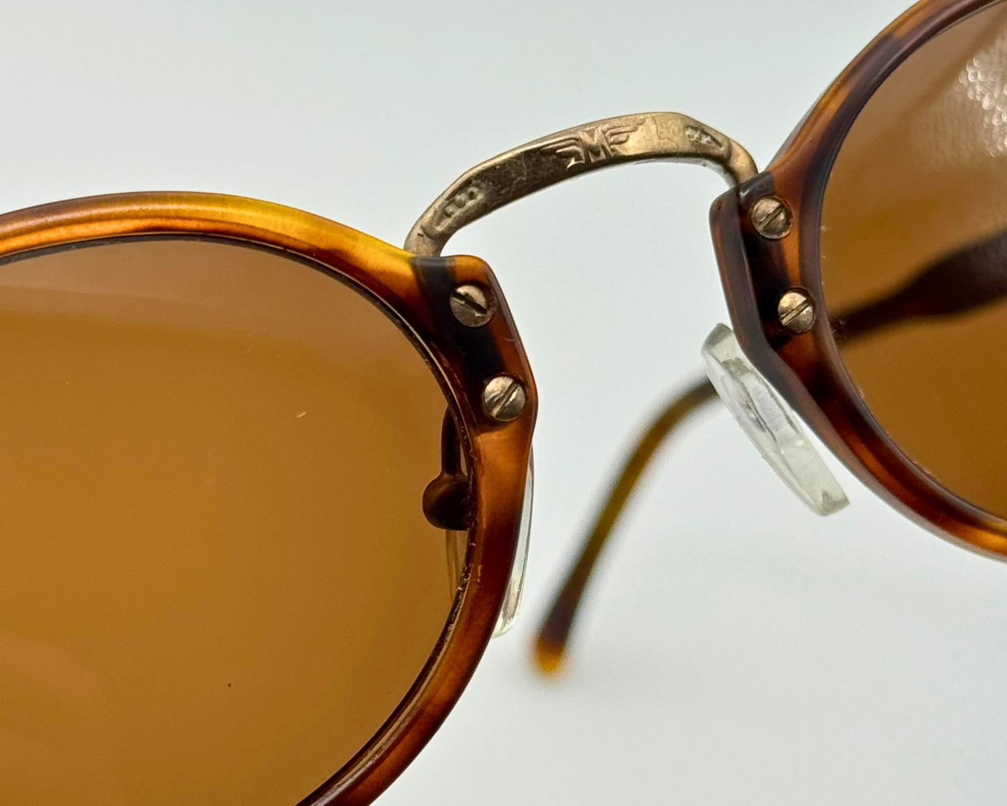 Close-up of the tortoiseshell pattern and metal hinge details on vintage 1990s round sunglasses with new brown lenses.