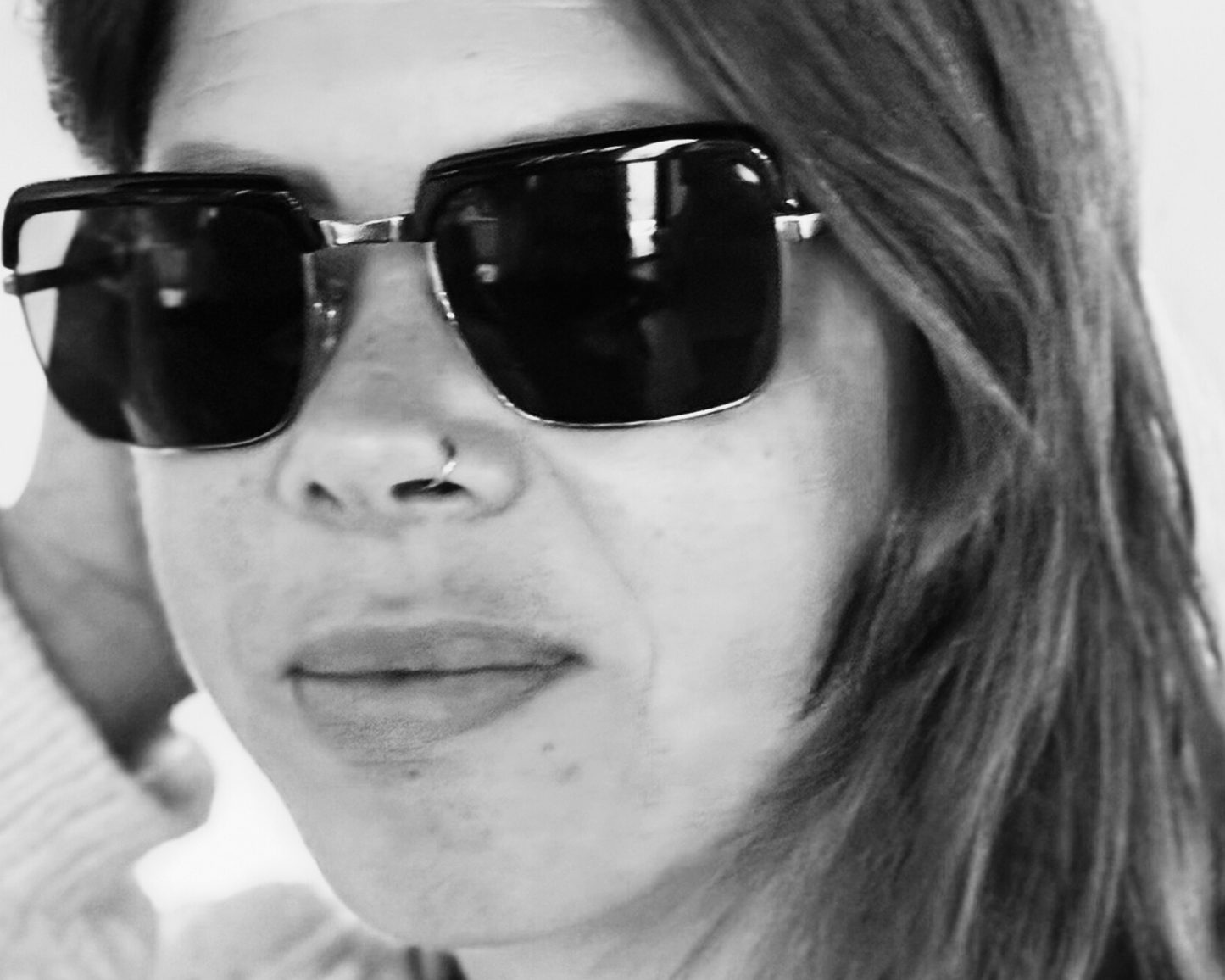 A black and white photo of a person wearing square-shaped sunglasses.