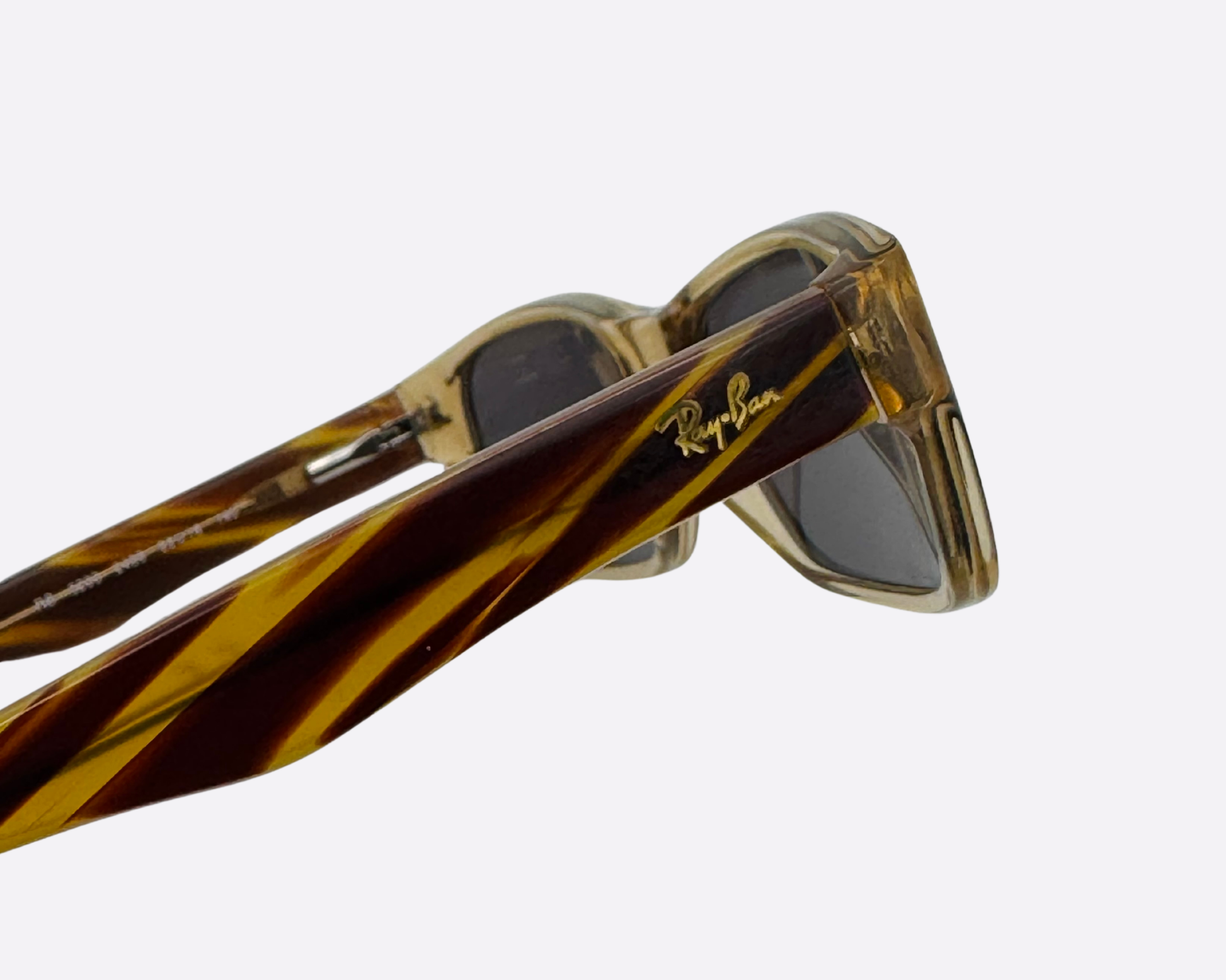 Close-up of the gold Ray-Ban logo on the striped temple of a pair of designer sunglasses.