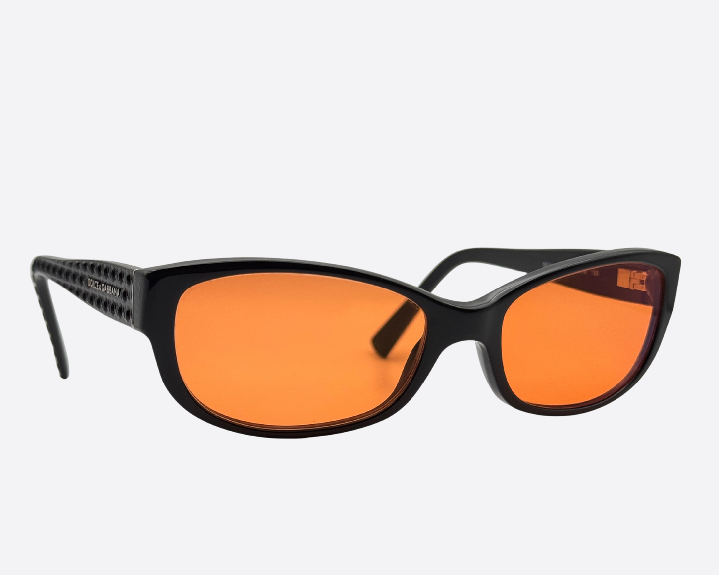 Angled view of the Dolce & Gabbana DG3125 sunglasses. The black frame features a textured, patterned temple on the left side and new orange lenses.