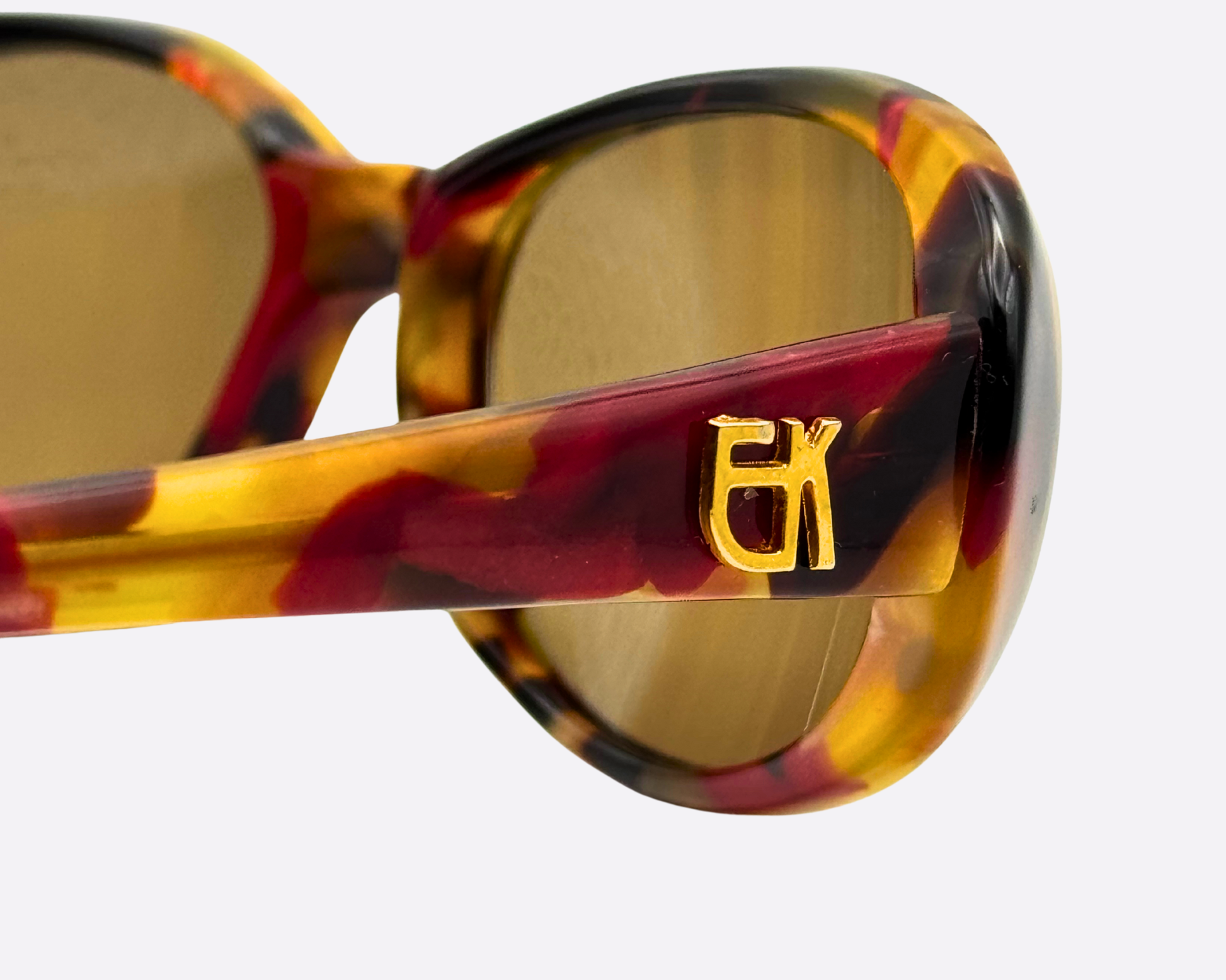 Close-up of the iconic gold Emmanuelle Khanh "EK" logo on the side of the red and brown marbled acetate frames, highlighting the luxurious 90s couture texture.