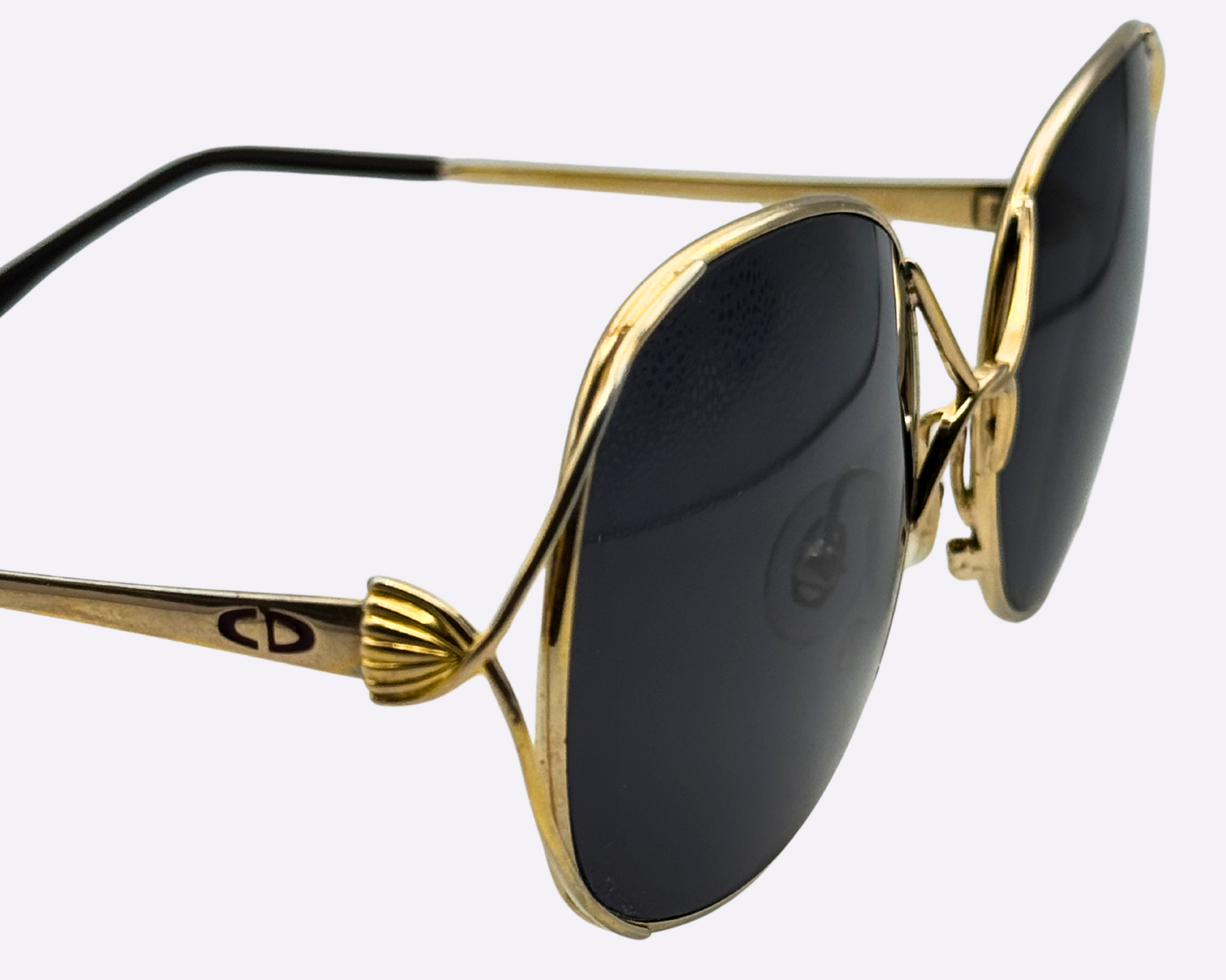 Close-up of the temple and Dior logo on vintage 1980s Christian Dior sunglasses with a steel frame and new grey lenses, shown on a light gray background.