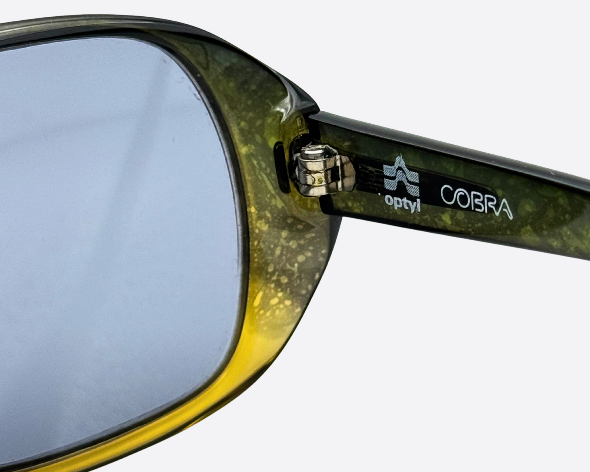 Macro shot of the Cobra brand logo and Optyl trademark on the inner side of the translucent green frame, highlighting the authentic 1970s designer details.