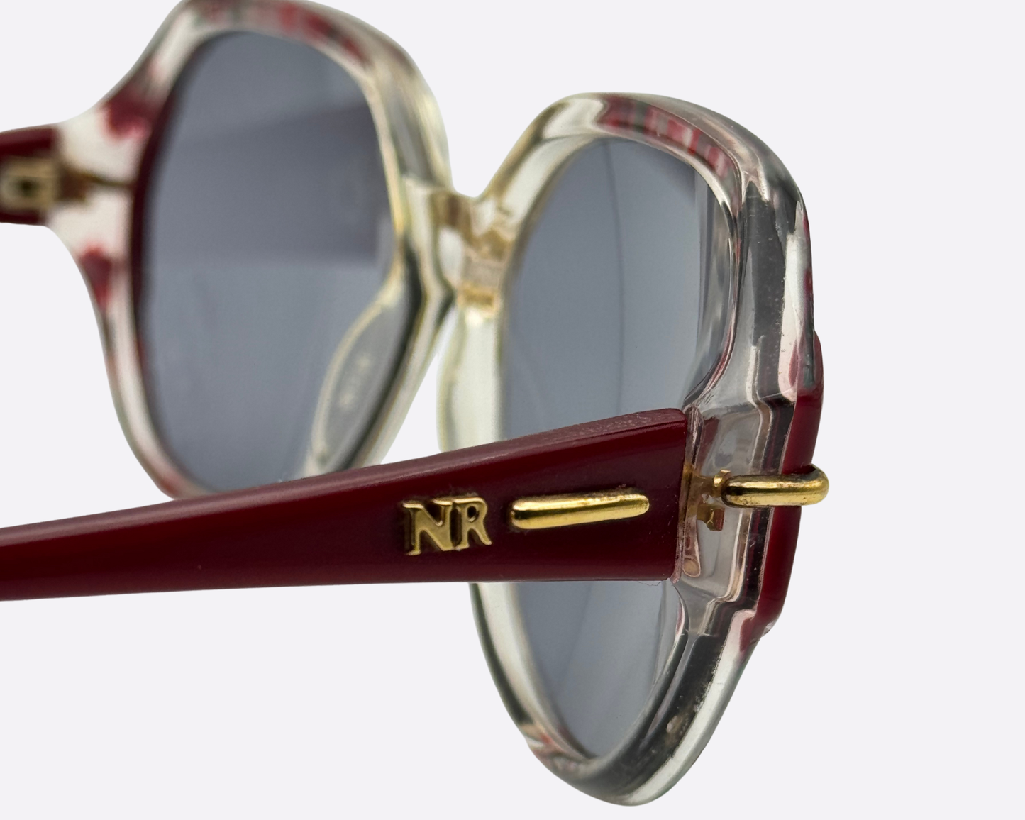 Close-up of the Nina Ricci logo on the side temple of model 2406 sunglasses, featuring vibrant red and pink patterned arms and translucent geometric frames, vintage French couture luxury eyewear
