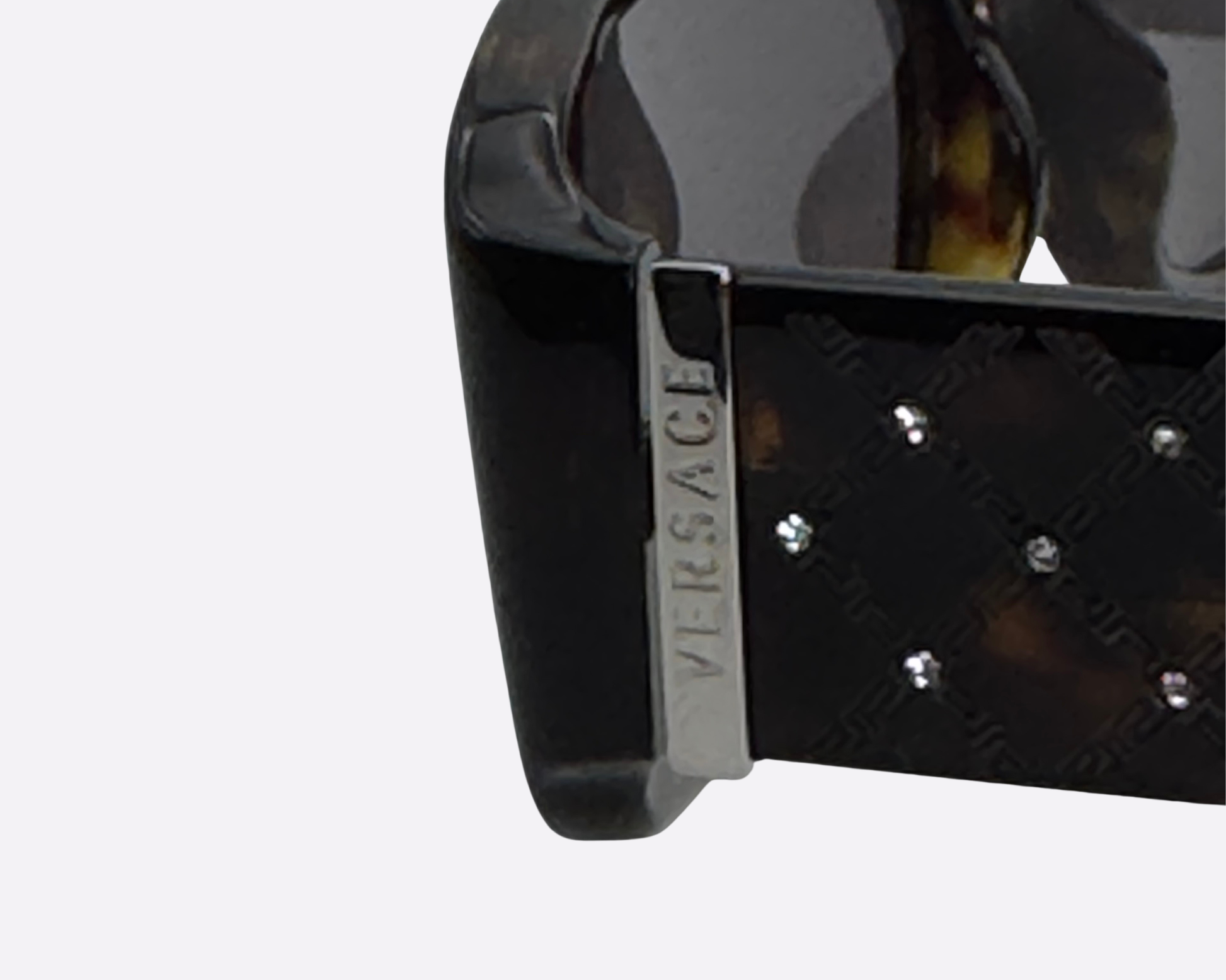 Close-up of the silver Versace logo on a dark tortoiseshell temple with a textured diamond pattern.
