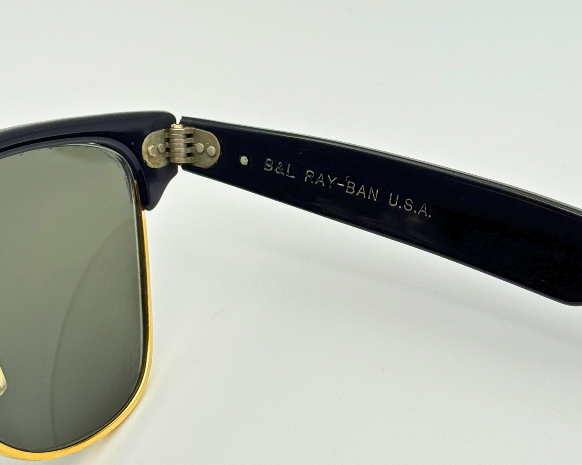 Close-up of a Ray-Ban sunglasses with 'S&L Ray-Ban U.S.A.' engraving on the arm against a white background.