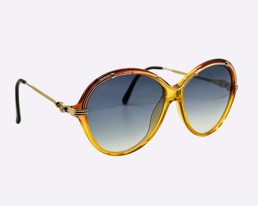 Side view of vintage 1980s Christian Dior sunglasses, model 2251 30, made in Austria, with a gold and red frame in a metal and optyl mix and new grey gradient lenses, shown on a light gray background.