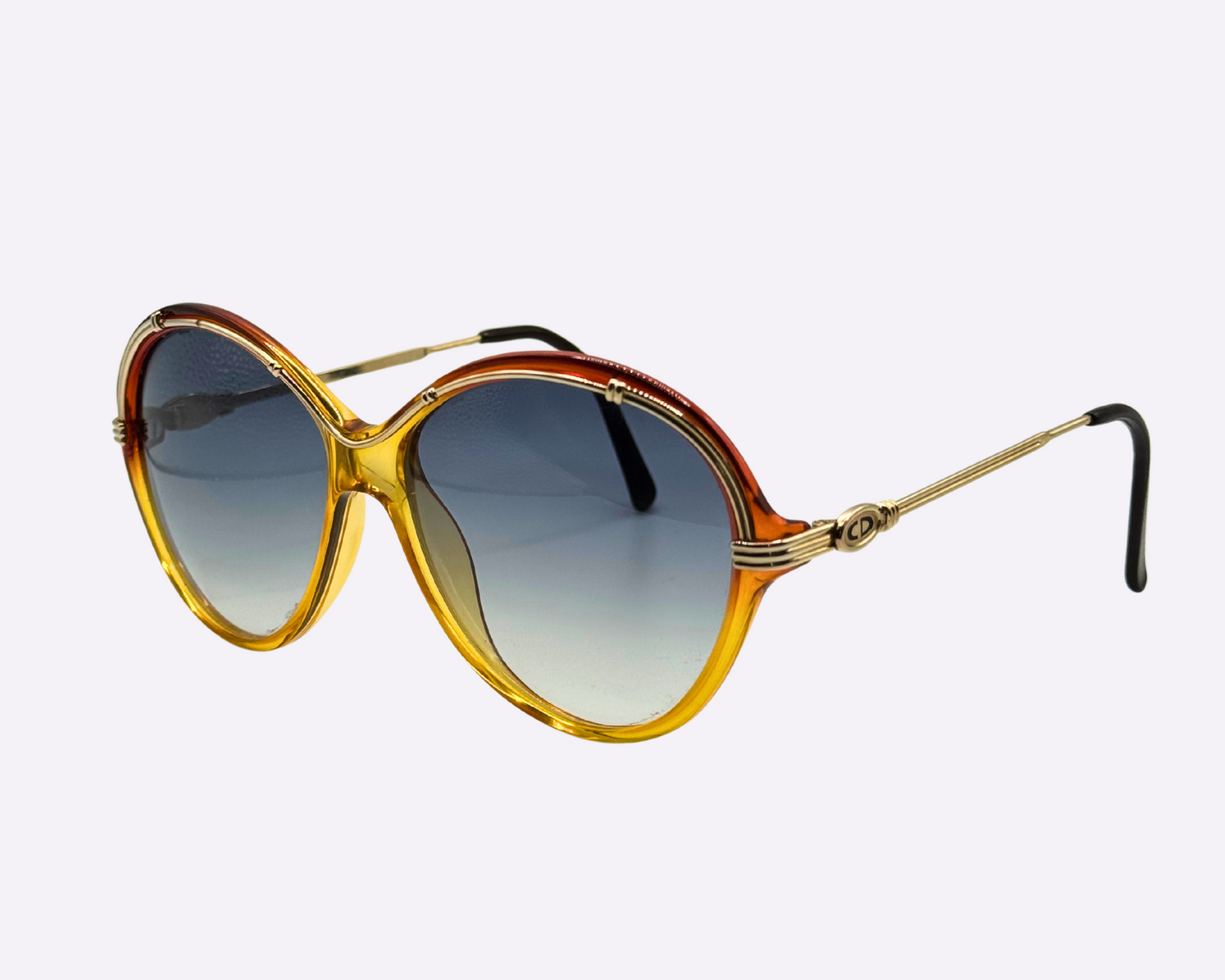Side view of vintage 1980s Christian Dior sunglasses, model 2251 30, made in Austria, with a gold and red frame in a metal and optyl mix and new grey gradient lenses, shown on a light gray background.