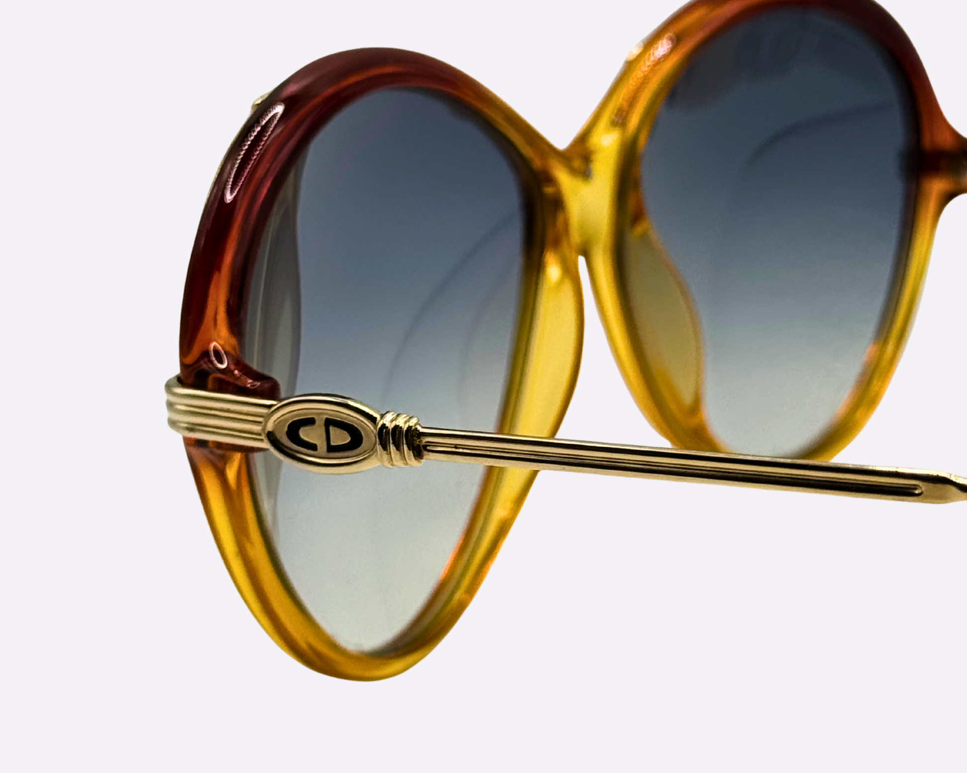 Close-up of the temple and Christian Dior logo on vintage 1980s sunglasses, model 2251 30, made in Austria, with a gold and red frame in metal and optyl and new grey gradient lenses, shown on a light gray background.